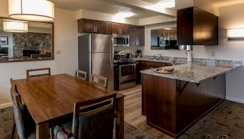 A modern kitchen and dining area featuring stainless steel appliances, wooden dining table with chairs, and granite countertops.