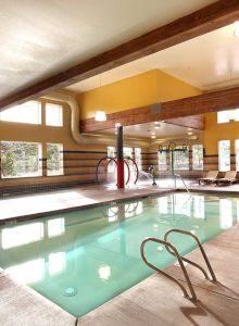 An indoor pool area with lounge chairs, windows, a water slide, and various overhead lights can be seen.