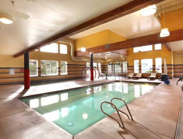 An indoor pool area with lounge chairs, windows, a water slide, and various overhead lights can be seen.