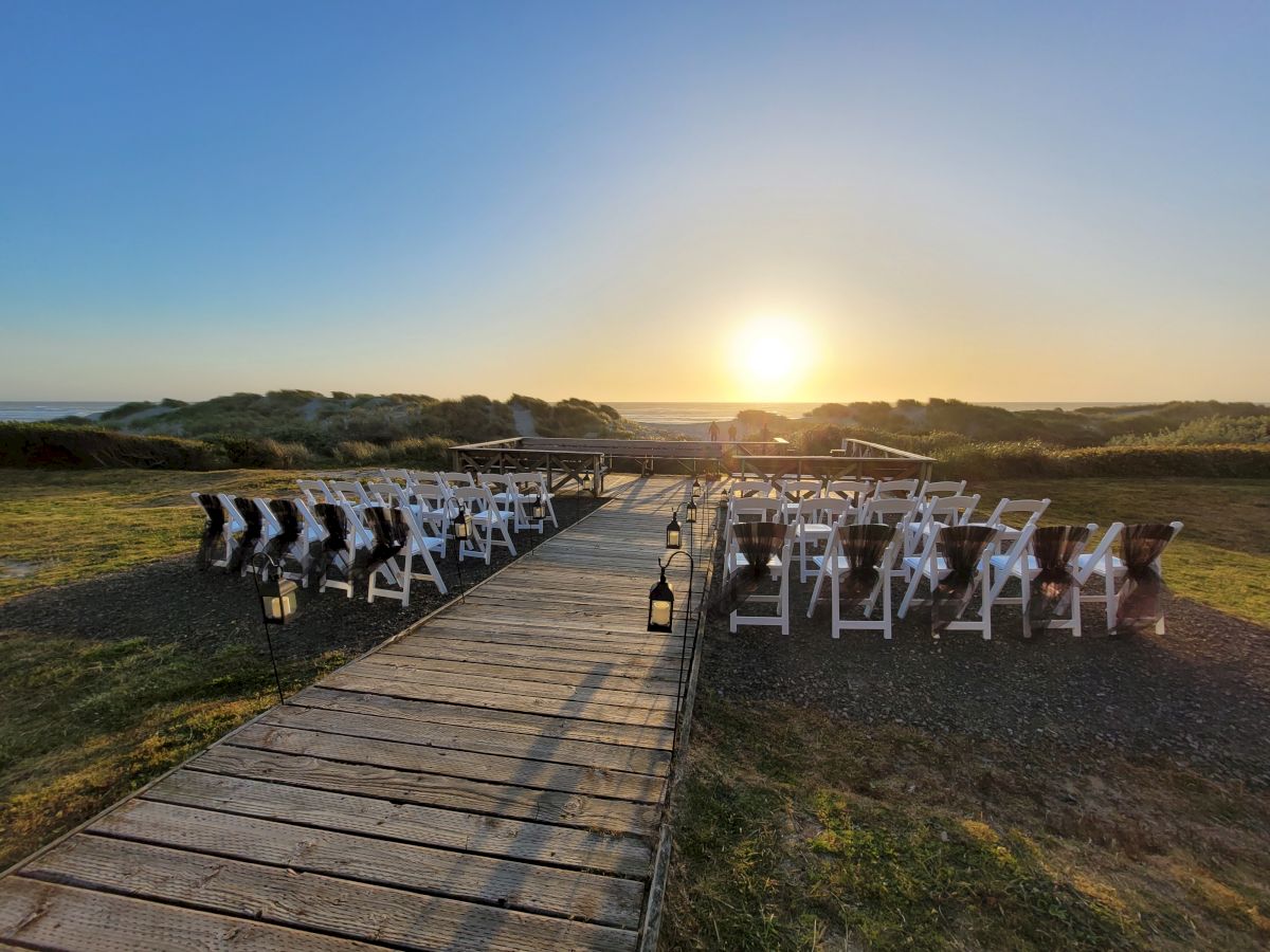 A sunset view over a walkway leading to an outdoor setup with white chairs arranged on either side, likely for an event or ceremony.