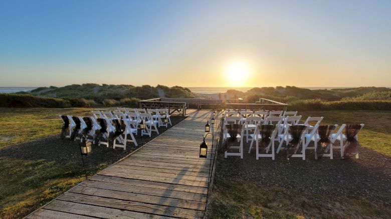 A sunset view over a walkway leading to an outdoor setup with white chairs arranged on either side, likely for an event or ceremony.