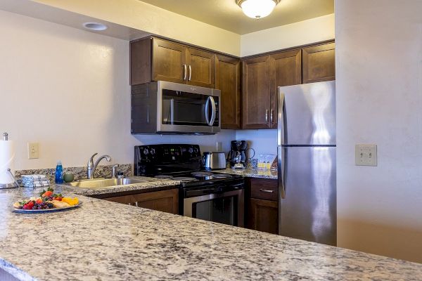 A modern kitchen with granite countertops, wooden cabinets, stainless steel appliances, and a fruit plate on the counter.