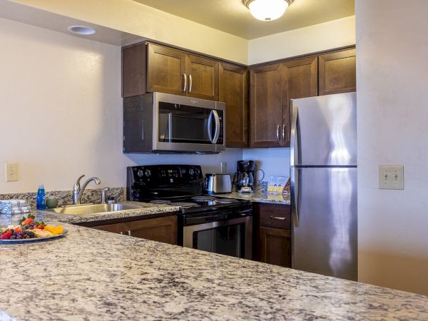 A modern kitchen with granite countertops, wooden cabinets, stainless steel appliances, and a fruit plate on the counter.