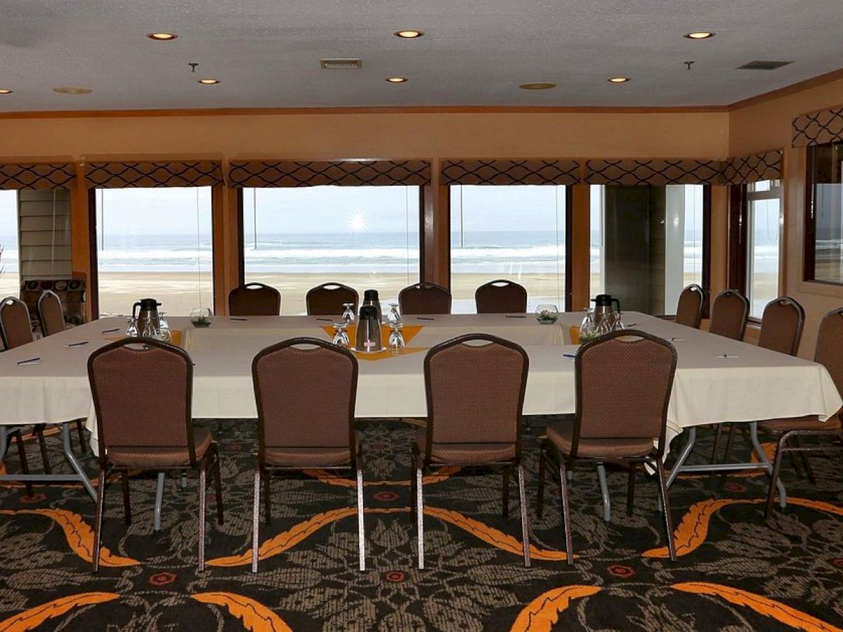 A conference room with a large table, chairs, and a view of the ocean through windows. The table has water pitchers, glasses, and notepads.