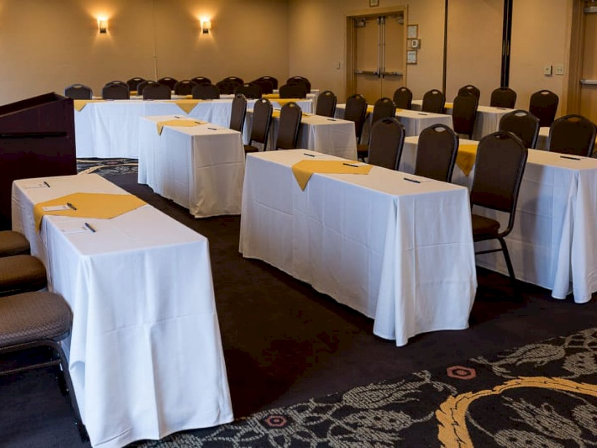 The image shows a conference or meeting room setup with rows of tables and chairs, covered in white tablecloths, and a podium at the front.