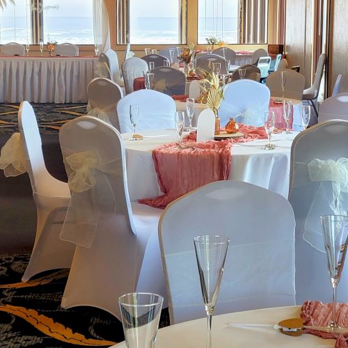 The image shows an elegantly decorated banquet hall with round tables covered in white cloth, champagne glasses, and pink accents, likely set for a wedding.