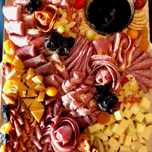 A charcuterie board with various meats, cheeses, crackers, dried fruits, and a bowl of dark dip, arranged aesthetically on a wooden surface.