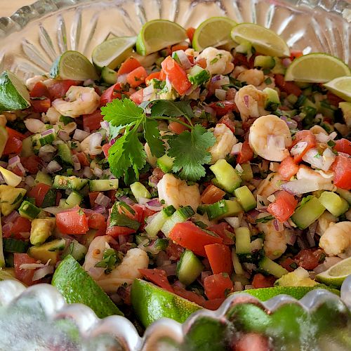 A glass bowl filled with a colorful seafood ceviche garnished with lime slices and cilantro.