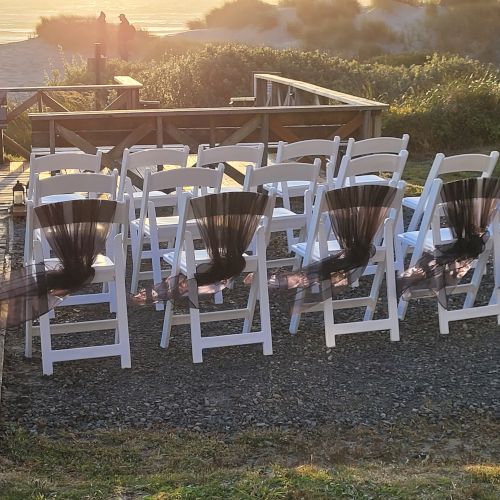 This image shows an outdoor setup for a wedding or event with decorated white chairs facing a scenic background.