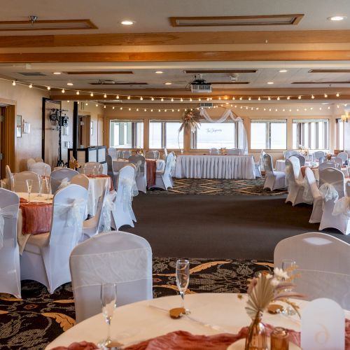 An elegantly decorated banquet hall with round tables, white chair covers, drapes, and string lights. It seems ready for a formal event or wedding.