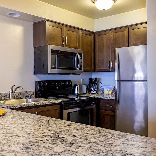 A modern kitchen with stainless steel appliances, granite countertops, and wooden cabinets, featuring a plate of fruit on the counter.