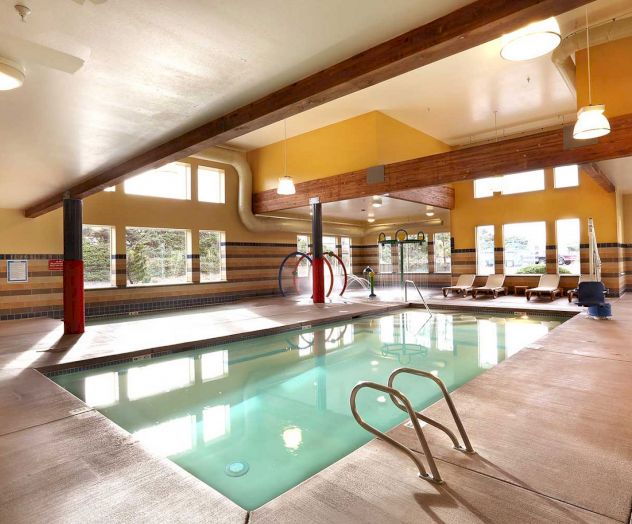 An indoor swimming pool area with lounge chairs, large windows, and modern lighting, creating a bright and inviting atmosphere.