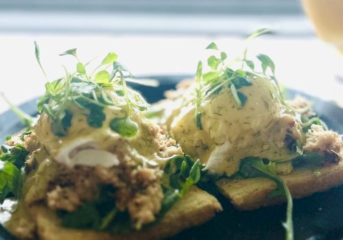 Two toasted crackers with creamy topping and fresh herbs on a dark plate, artfully arranged by the seaside.