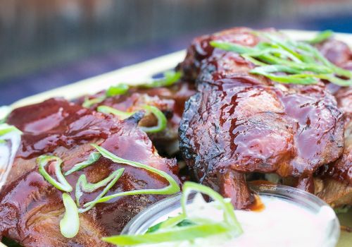 A plate of glazed barbecued ribs with green onion garnish and a dipping sauce, close-up and appetizing.