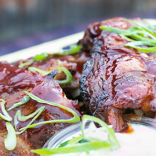 A plate of glazed barbecued ribs with green onion garnish and a dipping sauce, close-up and appetizing.