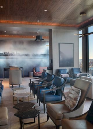A modern lounge area with comfortable seating, city skyline art, large windows showcasing a waterfront view, and a ferris wheel in the distance.