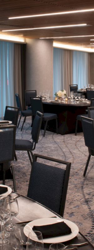 The image shows an elegantly set dining room with several round tables, each adorned with black napkins, glasses, and floral centerpieces.
