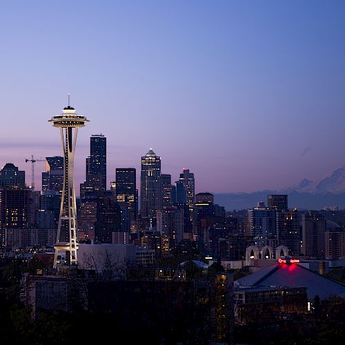 This image shows the Seattle skyline at dusk, featuring the Space Needle, various high-rise buildings, and Mount Rainier visible in the background.